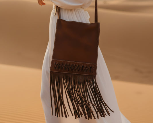 Front view of the Nomad Trail leather crossbody bag in walnut brown with long leather fringe and handcrafted woven leather pattern

Close-up of the handcrafted leather weaving detail on the Nomad Trail walnut leather crossbody bag

Lifestyle image of the Nomad Trail walnut leather fringe crossbody bag worn crossbody
